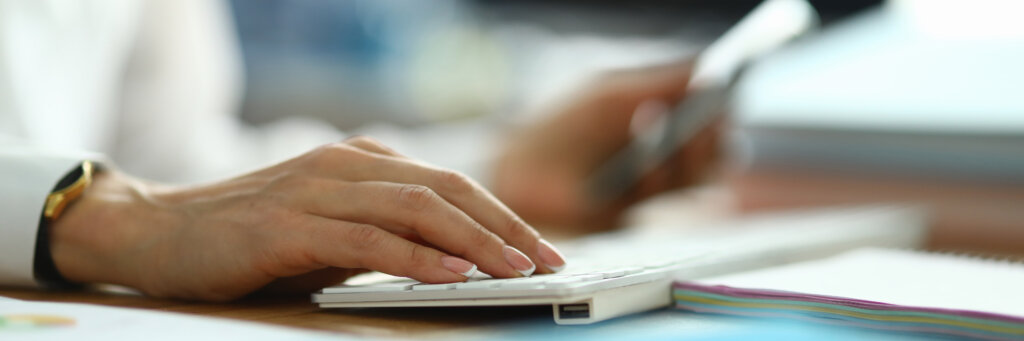 Woman in white coat hold her hand on white keyboard and type text.